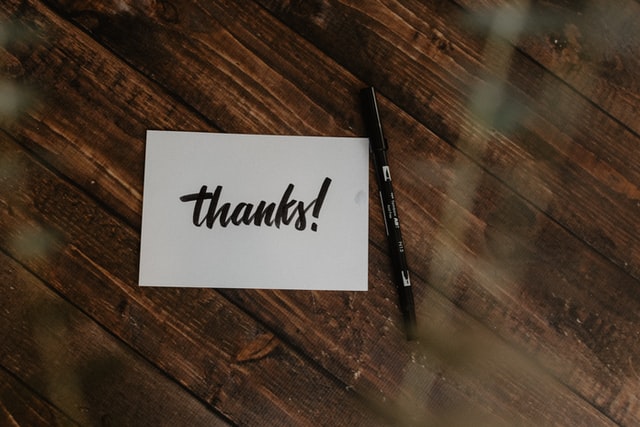 A thank-you note and a pen sitting on a rustic wooden table.