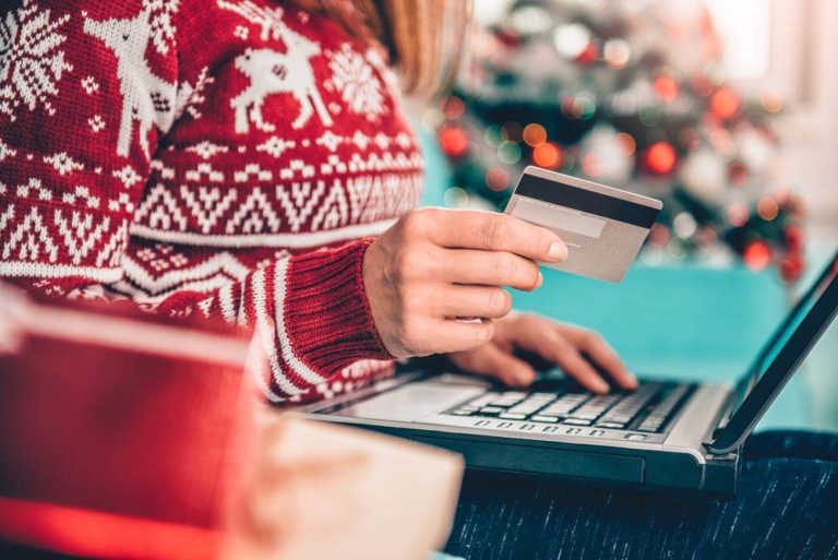 Woman in a red Christmas sweater holding a credit card in one hand as she shops online