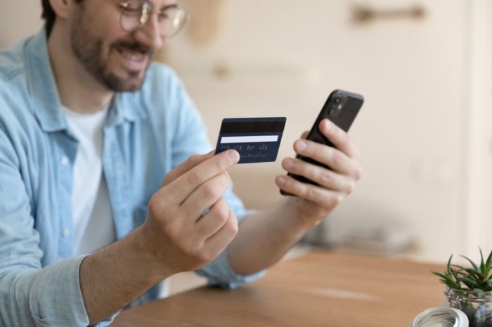 A young man holds up his credit card to make an online payment from his phone