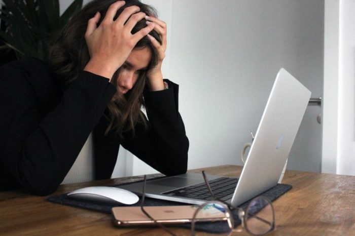 A stressed woman holds her head while staring at her computer screen